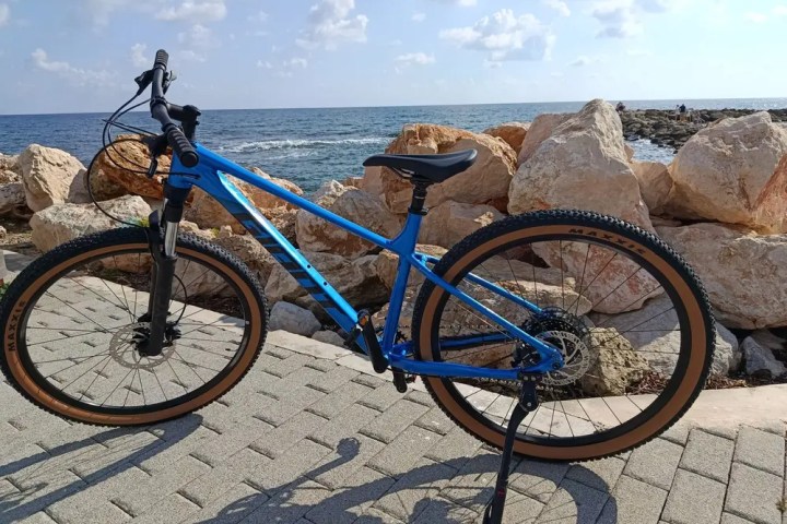 Blue mountain bike parked on a stone path by the sea with large rocks in the background.
