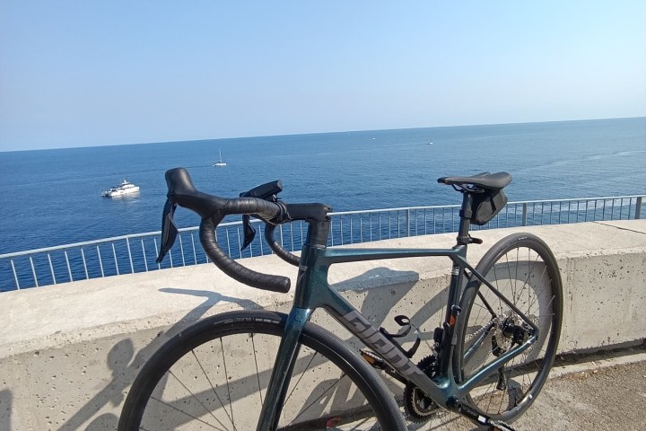 Bicycle parked by a seaside railing with boats in the distance.