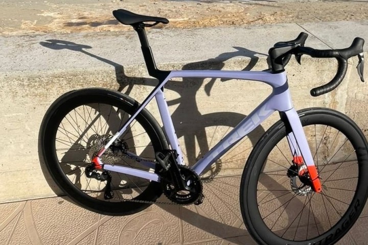 A sleek purple road bike leaning against a concrete wall.
