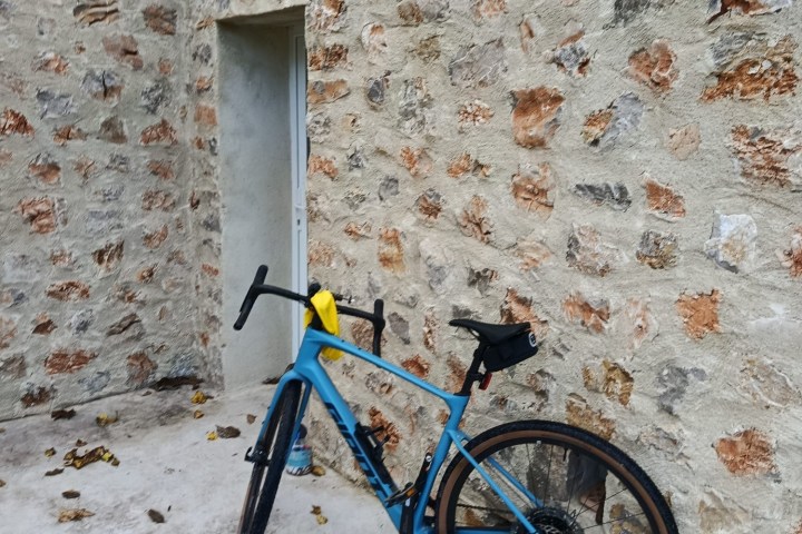 Blue bicycle leaning against a textured stone wall on a concrete floor.