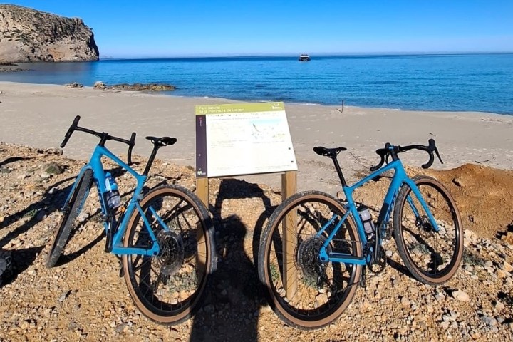 Two blue bicycles parked on a beach with a clear sea and blue sky in the background.