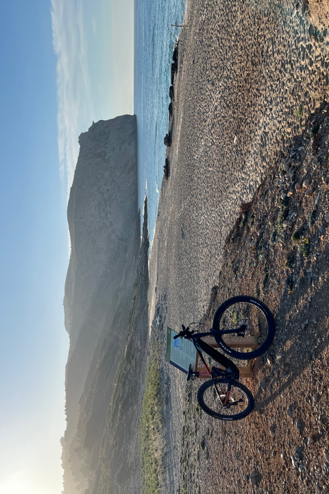 Bicycle on a rocky beach with mountain and ocean view at sunset.