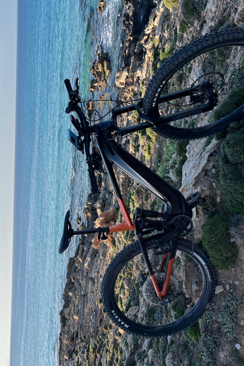 Mountain bike on rocky coastal path beside a blue sea under a clear sky.