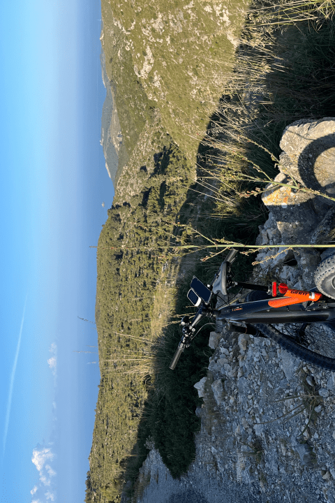 Mountain bike on rocky hill overlooking distant sea and clear blue sky.