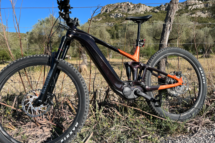 Orange and black mountain bike with large tires parked by a wire fence and rocky hills in the background.