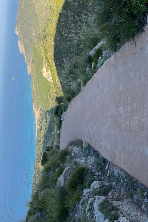 Bicycle handlebar view on mountain path overlooking ocean and cliffs.