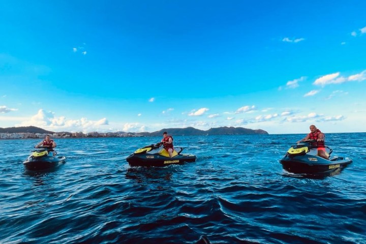 Three people on jet skis on a vast blue sea with a clear sky.