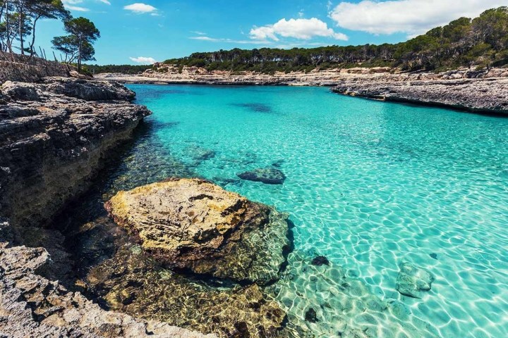 Clear turquoise water in a rocky coastal cove under a blue sky.