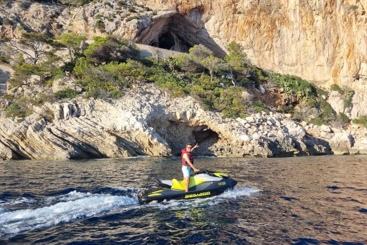 Person riding a jet ski near a rocky coastline with cliffs and greenery.