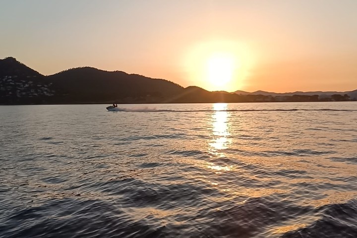 Jet ski on a calm sea at sunset with silhouetted hills in the background.